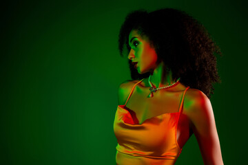 Elegant young woman in a satin dress posing artistically with a green backdrop and vibrant lighting...