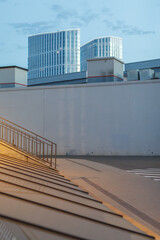 Minimalist cityscape with tall modern glass towers behind a plain concrete wall at sunset. Urban contrast between architecture and infrastructure in soft evening light.
