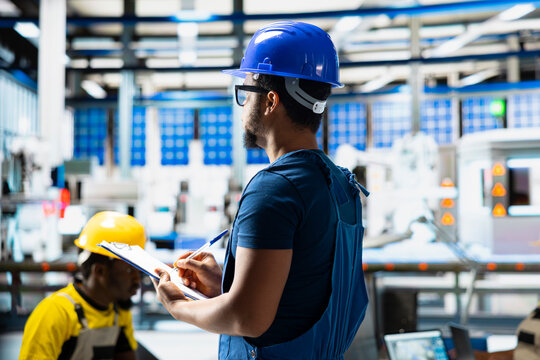 African american supervisor evaluates renewable energy metrics at factory, using advanced monitoring and manufacturing tools on files. Engineer improves solar power system accuracy.