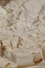 Close-up of soft white fabric with deep folds lying on a bed in warm natural light. Ideal for backgrounds, fabric textures, bedding ads, calm mood, minimal interior concepts.
