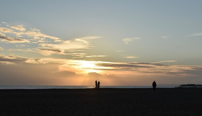 People are walking at the beach during sunset