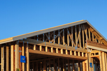 A wood-framed residential structure under construction shows roof trusses, support beams, and framing connectors, illustrating early-stage homebuilding with structural elements exposed