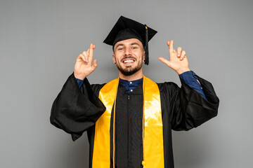 Hopeful graduate crossing fingers wearing mortarboard and gown