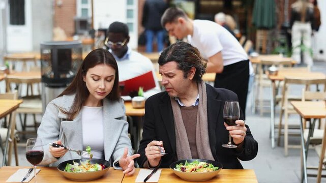 Girl in cafe sits near male companion, has nice conversation and discusses news of day. Cozy atmosphere of cafe, meeting place for friends, business partners, colleagues.