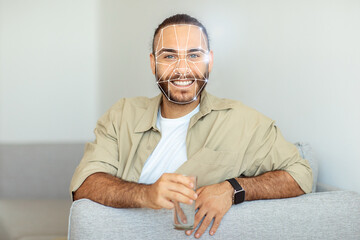 A person comfortably sits on a couch, enjoying a drink while engaging with facial recognition...