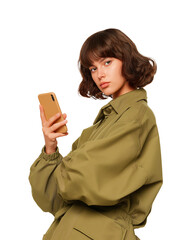 Stylish brunette woman is holding a mobile phone and looking at the camera with an attitude she is wearing a trendy olive green jumpsuit against a plain transparent background