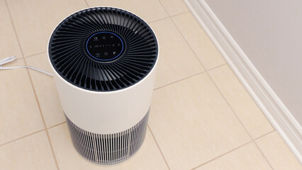 Tall round air purifier with a black top fan and a white body on a tile floor against the wall