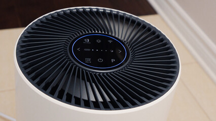 Tall round air purifier with a black top fan and a white body on a tile floor against the wall