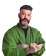 Stylish tattooed man with beard and modern hairstyle posing confidently while holding a smartphone and wearing a green bomber jacket against a plain background in a studio setting