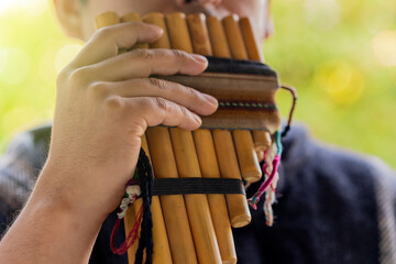 Close up of a young Andean man playing zampoña, a traditional Andean musical instrument.