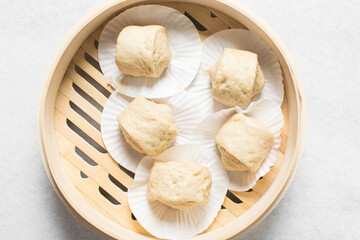 Overhead view of steamed bun dough in a steamer basket, top view of mantou dough in a bamboo steamer, process of making steamed milk buns