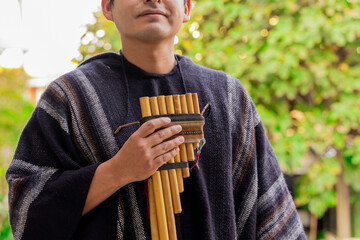 Man in traditional Andean clothing playing pan flute outdoors

