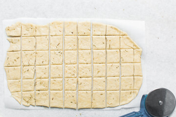 Overhead view of crackers dough on parchment paper, cutting cracker biscuit dough on white...