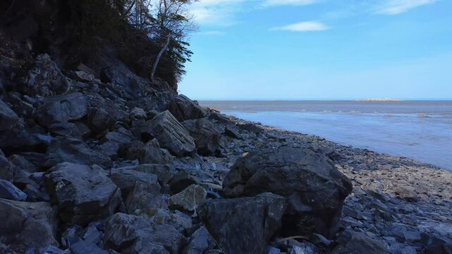 Low‑altitude drone footage of the rocky shoreline of Mitis Bay with the blue sky meeting the horizon along the St. Lawrence River in Quebec, Canada, 2025.