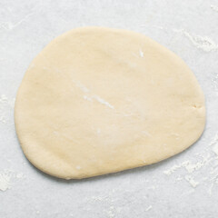 Overhead view of doughnut dough being rolled on a white countertop, top view of doughnut dough on a white countertop, process of making doughnut