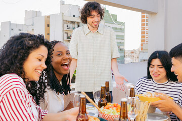 Young black woman laughs on camera with her latin friends, at lunch on terrace at noon