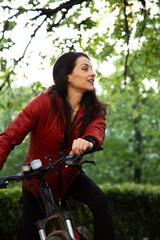Beauty smiling woman in sport jacket and long brown hair biking on bicycle on spring trees...