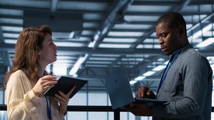 Colleagues in data center workplace use laptop to calibrate energy usage. Server farm IT specialist using notebook to inspect UPS configurations, doing maintenance on equipment, camera A