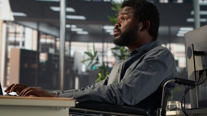 African american male worker in wheelchair trying to solve daily tasks at the office, examining...
