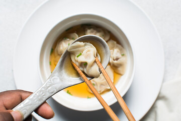 Overhead view of wonton in a ceramic spoon, clear soup with dumplings in a ceramic spoon