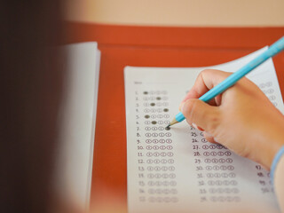 Closeup of female student's hand doing exam in classroom. School proficiency test. Asian student doing exam. Education, learning