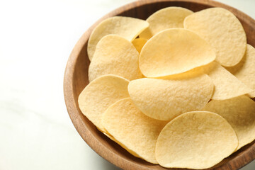 Tasty potato chips in bowl on white marble table, closeup