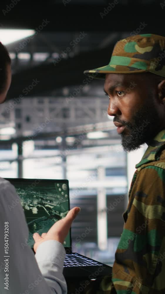 Poster vertical video army operators in data center using laptop to run drone control software, looking at 