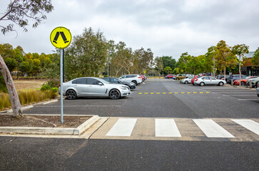 A public parking lot featuring a marked pedestrian crossing, warning sign, and parked vehicles in Australia. Concept of road safety infrastructure,organized public space design and car park amenities. © Doublelee