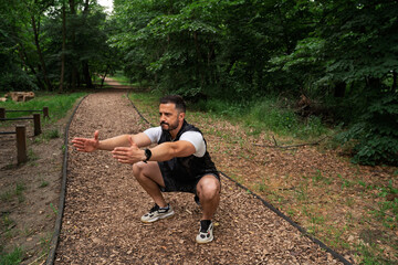 Handsome muscular man doing squats in the nature 