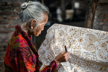 Indonesian artisan drawing traditional batik pattern on fabric