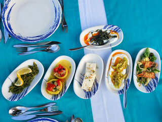 Assortment of Mediterranean appetizers served on blue tablecloth. Various dishes with vegetables and cheeses in oval plates, ready for eat. Top view. 