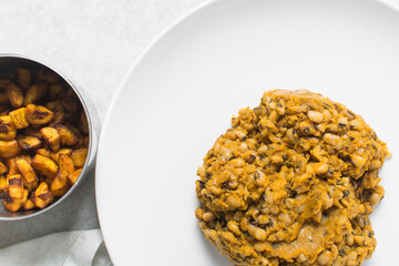 Overhead view of nigerian fried beans and fried plantain on a white plate, top view of nigerian stewed beans and plantain on a white background
