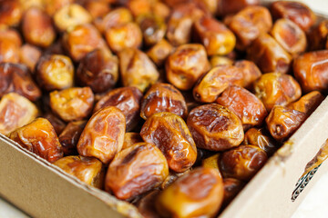 Close-up of assorted dried dates, showcases their varied textures and amber tones, elegantly arranged in a cardboard container, ideal for healthy snack and culinary-themed visuals.