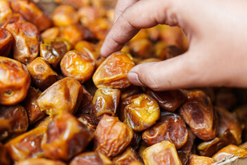 A hand reaches into a pile of glistening, fresh dates, highlighting their rich color and texture. The image evokes a sense of natural sweetness and healthy indulgence, perfect for a snack.