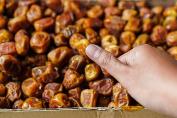 A hand selects from a pile of sweet dates, showcasing a focus on organic healthy snacking. Perfect for nutrition, a treat for mindful eating, and a sweet dessert.