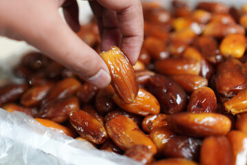 Close-up showcases a person's hand selecting a glistening, caramel-colored date from a plentiful...