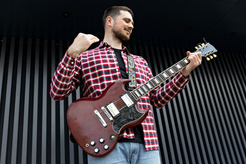 A stylish young guy plays the guitar on a dark background