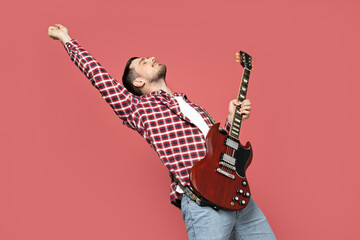 Attractive young guy playing the guitar on a pink background