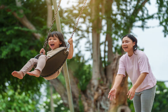 cheerful toddler girl with mother playing on a swing at playground