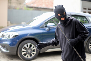 Burglar Dressed in Dark Clothing Targeting Parked Vehicle in Daylight Car Park.