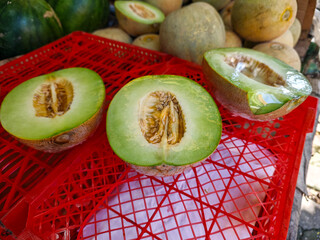 A vibrant still life features halved green melons with visible seeds on a red plastic basket,...