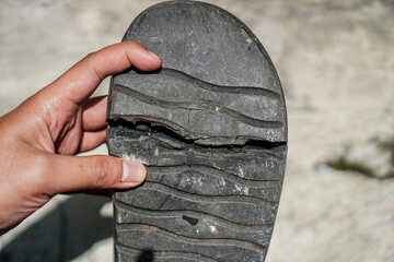 A worn and broken sandal sole held by hand, showcasing damage and wear. The textured rubber reveals...