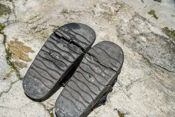 Worn black sandals with textured soles rest on weathered concrete, showcasing age and wear; ideal for themes of simplicity, resourcefulness, and everyday life with high definition capture.