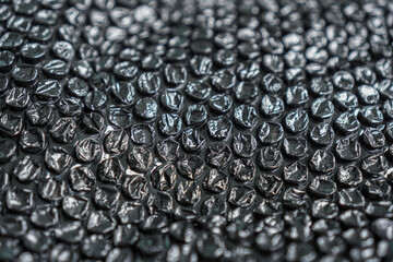A high angle close-up captures the abstract texture of black bubble wrap, creating a visually intriguing pattern, perfect for backgrounds or illustrating protective packaging solutions and logistics.