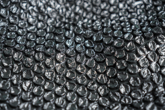 A high-angle close-up showcases a protective layer of dark bubble wrap, ideal for packaging or abstract designs, providing a cushioning texture that offers a versatile background element.