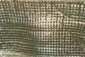 A shimmering silver surface displays a complex grid of textured squares, catching light and shadow...