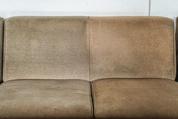 Detailed view of a brown, textured sofa showcasing signs of heavy use and varying degrees of cleanliness; it is suited for illustrating cleaning processes or product efficacy against stains.