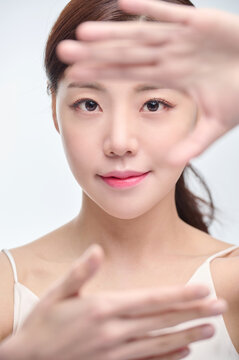 Young Asian Woman with Hands Framing Face in Minimal Studio