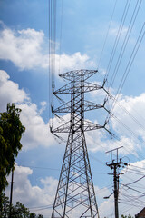 A tall electricity pylon rises against a blue sky dotted with soft clouds, symbolizing power and...