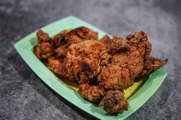 Crispy fried chicken pieces, perfect for comfort food advertisements or restaurant promotions, presented on a green plate over gray backdrop, ready to be enjoyed for lunch and dinner.